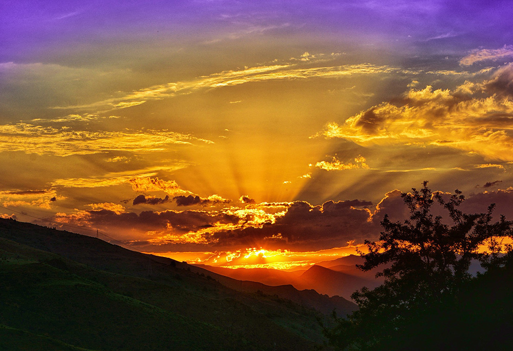 Photo illustration of a bright orange sunset shining through clouds, against a purple sky. (Pixabay/Rustu Bozkus)