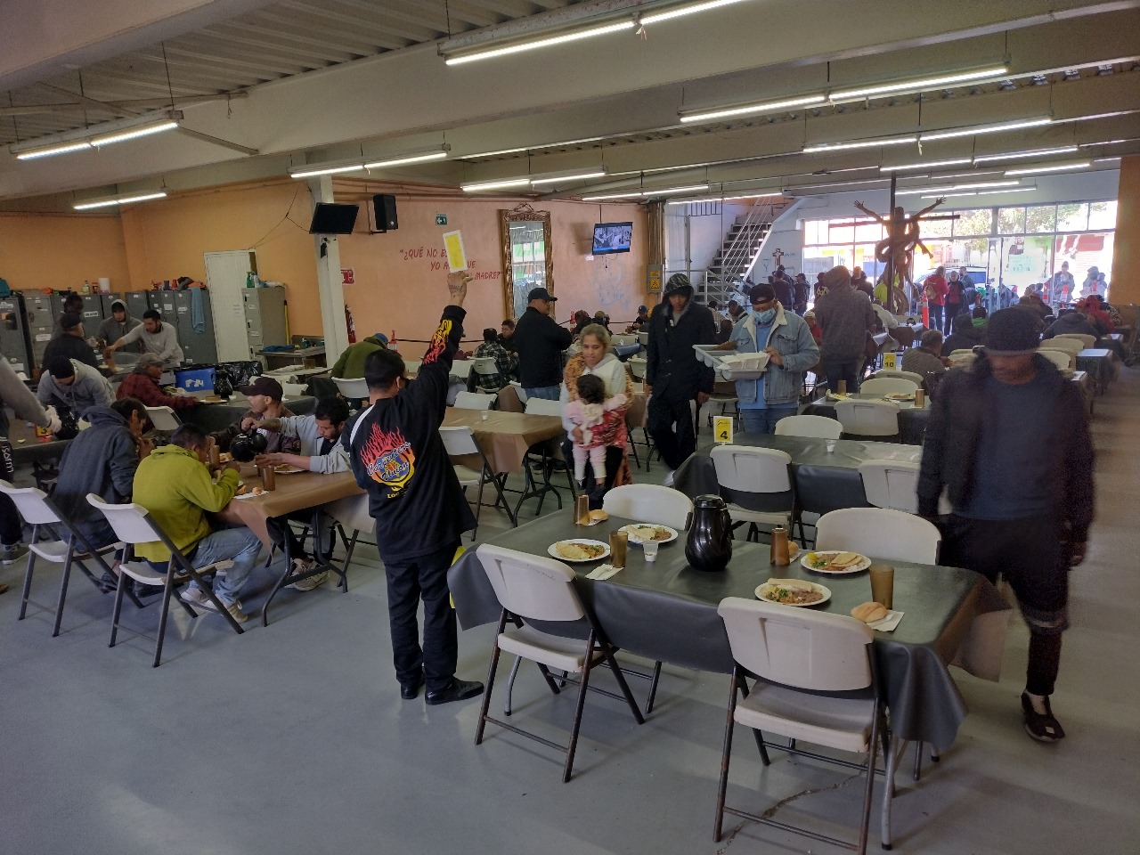 Durante las comidas en el Desayunador Padre Chava, uno de los migrantes levanta un cartel con un número para indicar cuál mesa está libre para que puedan pasar otras personas. (Foto: María Alejandra Leguizamón)