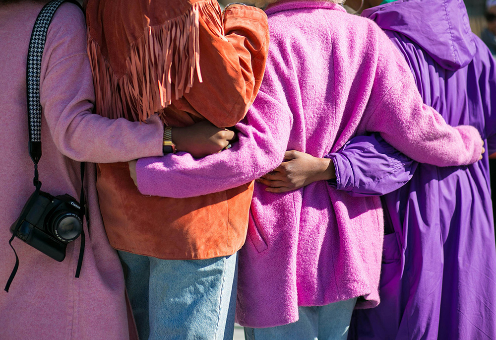 Women stand arm in arm outside (Unsplash/Vonecia Carswell)