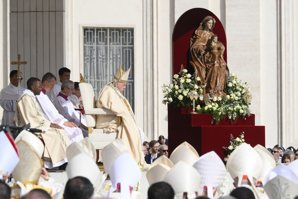 Pope Francis, vested, sits during Mass before statue. 