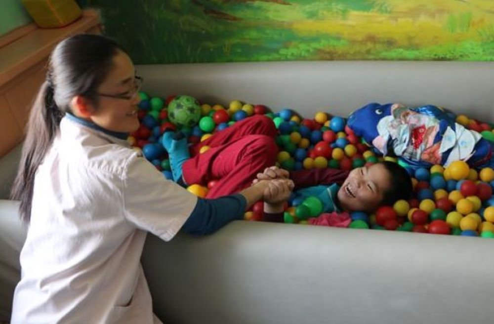 Sr. Magdalena works with a child in a tub filled with plastic balls,