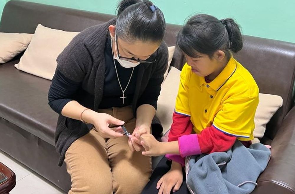 Sr. Magdalena trims the nails of a student with Down Syndrome.