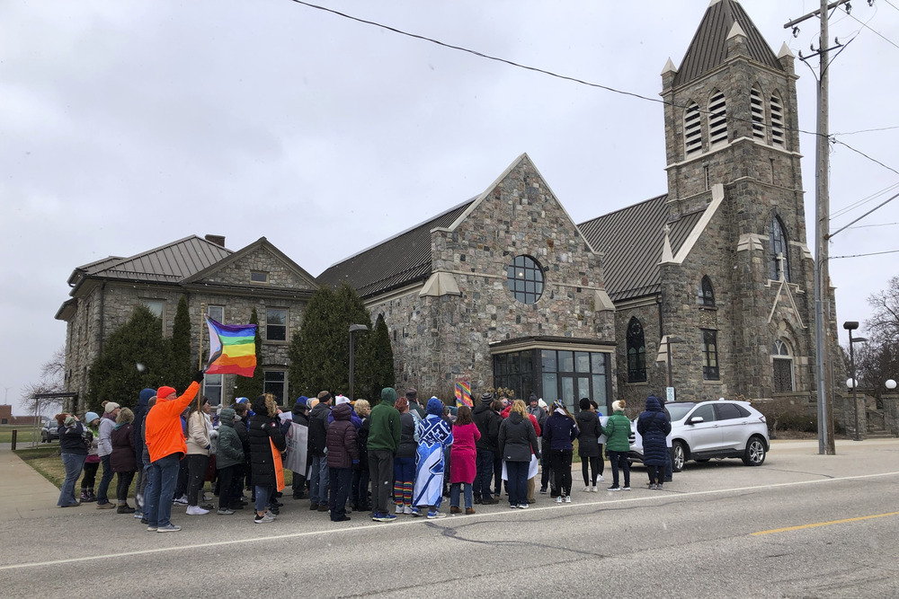 Protestors assemble outside stone church with pride flags