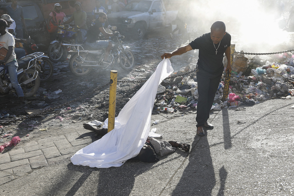 Person in street lifts white sheet amidst rubble and debris