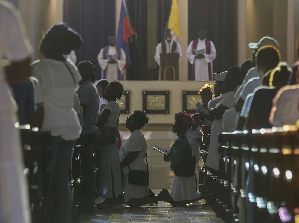 People kneel at pews and in aisle of church