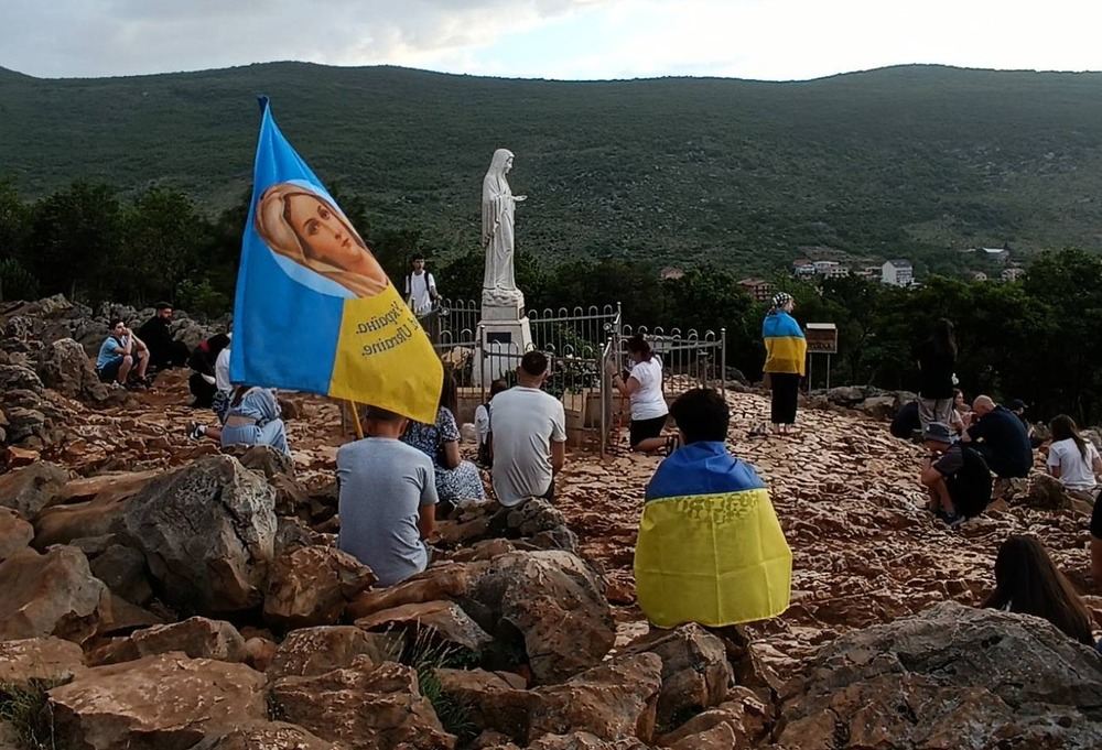 UKRAINE MEDJUGORJE PILGRIMAGE Children sit on rocky mound, draped in Ukrainian flags.