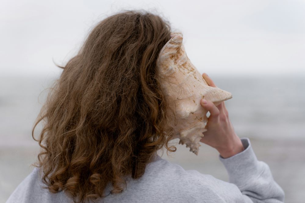 woman holds large shell to her ear