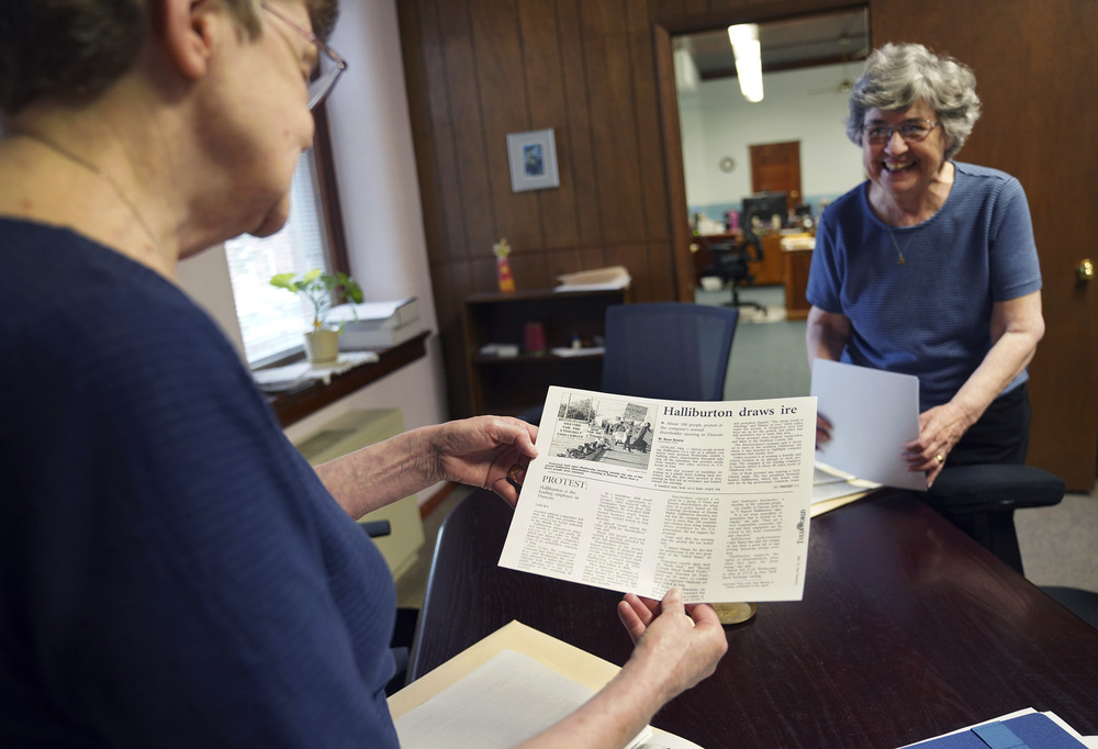Benedictine Srs. Rose Marie Stallbaumer and Barbara McCracken, Mt. St. Scholastica, Atchison, Kansas, July 16, 2024. The two sisters, wearing plainclothes, stand in wood-paneled office, looking at clippings and smiling.