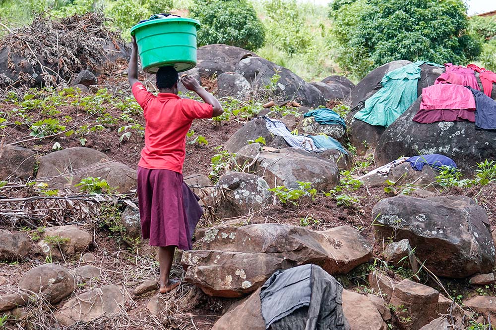 Ropa lavada en el arroyo de la aldea de Mpholiwa, en Malawi, el 15 de marzo de 2022, se seca extendida sobre piedras o en la hierba, mientras una niña espera para llevarla después a casa. (Foto: cortesía Mónica Ichife)