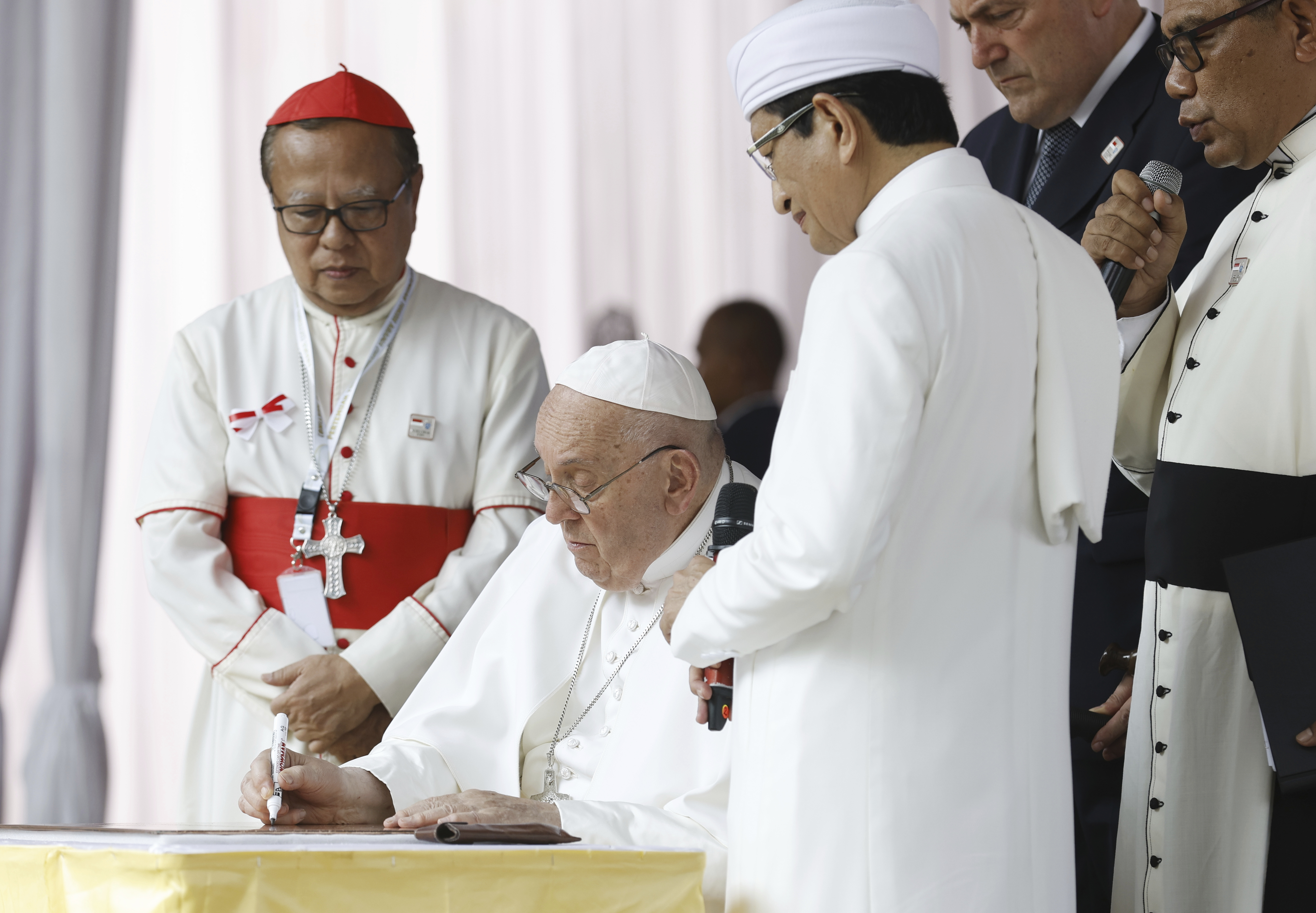 Pope Francis, center, flanked by the grand imam of Istiqlal Mosque Nasaruddin Umar, second right, and Archbishop of Jakarta Cardinal Ignatius Suharyo, left, signs a plate as he arrives at the Istiqlal Mosque for an interreligious meeting in Jakarta Thursday, Sept. 5, 2024. (Mast Irham/Pool Photo via AP) Pope Francis, center, flanked by the grand imam of Istiqlal Mosque Nasaruddin Umar, second right, and Archbishop of Jakarta Cardinal Ignatius Suharyo, left, signs a plate as he arrives at the Istiqlal Mosque for an interreligious meeting in Jakarta Thursday, Sept. 5, 2024. (Mast Irham/Pool Photo via AP)