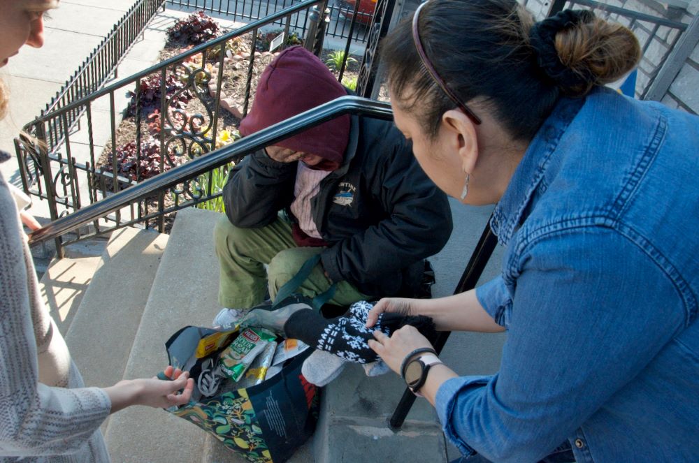 Olivia Sharkey and a staffer offer warm gloves and a hat to a neighbor suffering from the cold March air. il Olivia Sharkey and a staffer offer warm gloves and a hat to a neighbor suffering from the cold March air. iladelphia's Kensington neighborhood. (GSR photo/Dan Stockman)