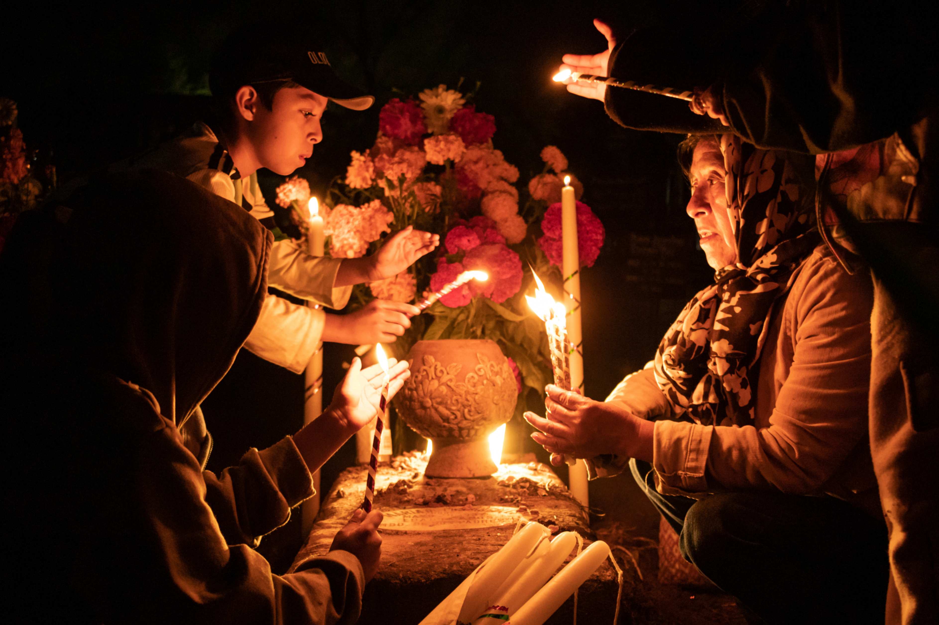 Unas personas sostienen velas sobre una tumba decorada con flores en un cementerio de Atzompa, México, a última hora del martes 31 de octubre de 2023. En una tradición que coincide con el Día de Todos los Santos, el 1 de noviembre, y el Día de los Difuntos, el 2 de noviembre, las familias decoran las tumbas con flores y velas y pasan la noche en el cementerio, haciendo compañía a sus seres queridos fallecidos. (Foto: AP/María Alférez)