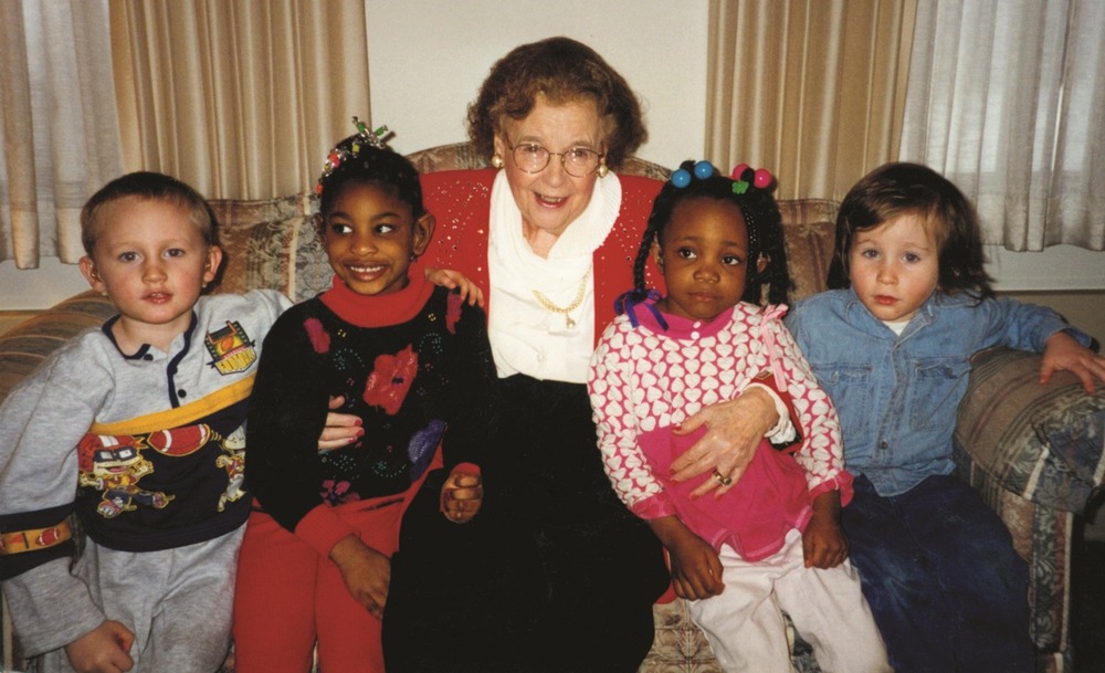 Dr. Gertrude Agnes Barber. Barber sits on a couch, smiling, with two children on each side.