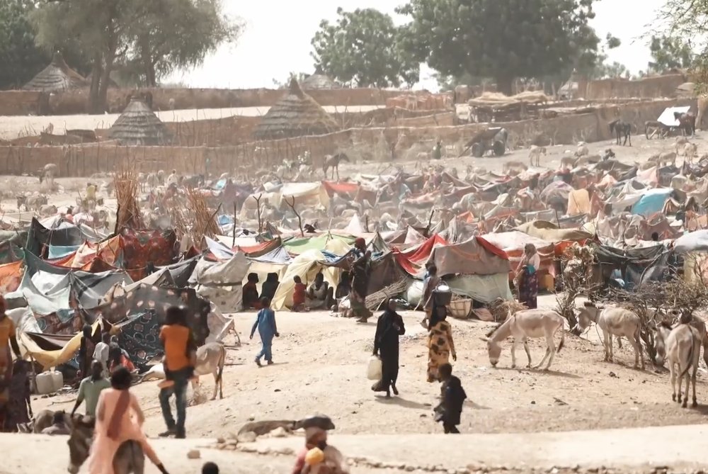 Sudanese refugee camp in Chad. View of many people walking and sitting among tents in dusty area.