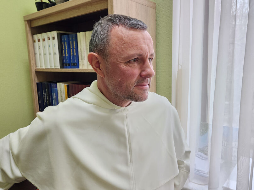Dominican Fr. Petro Balog. The priest stands wearing white habit staring out of window.