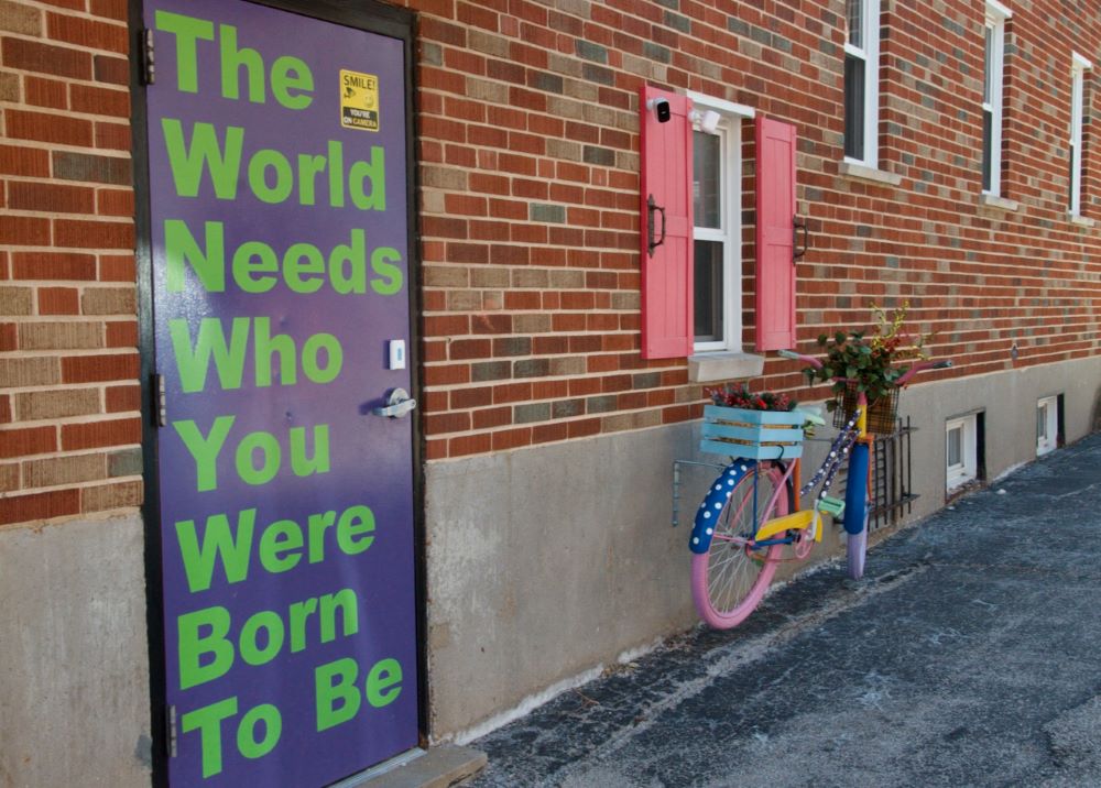 a sign on door and painted bike outside art center.