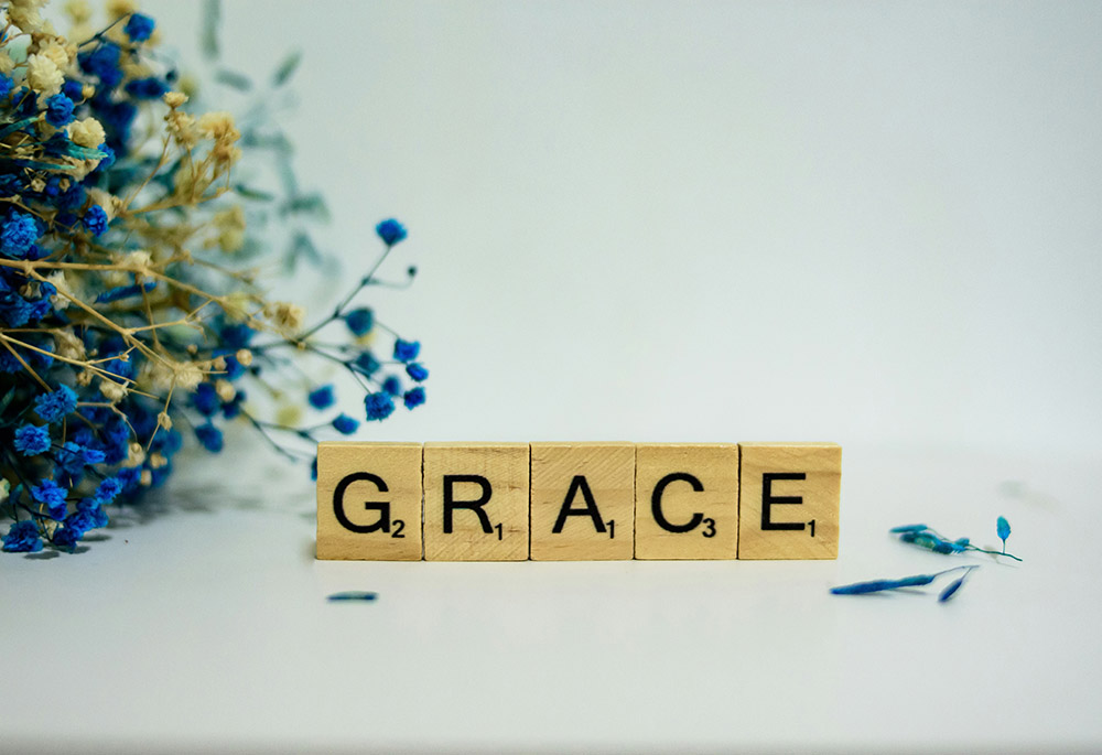 A row of wooden letters spell the word "grace," with a flower arrangement lying to its left. (Unsplash/Alex Shute)