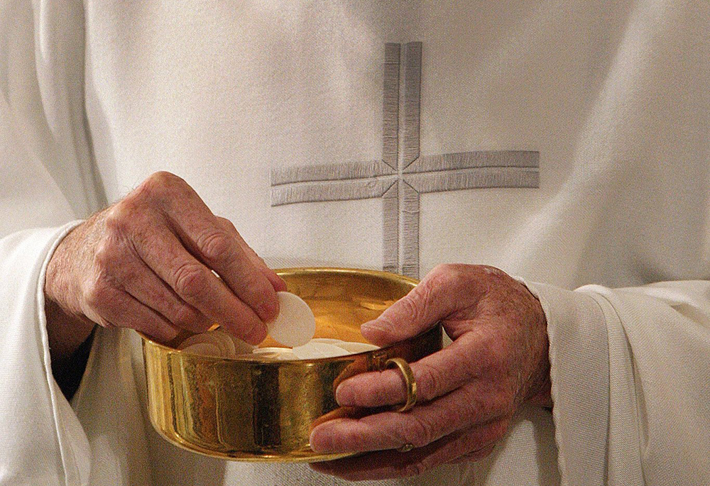 This photo illustration shows a priest preparing to distribute Communion during Mass. "Speaking from my experience and observations in two dioceses … I believe we can still talk about trust," writes Sr. Matilda Owolagba. "However, this trust does not extend to dioceses or institutions that do not have enough measures in place to prevent abuse." (OSV News/Bob Roller)