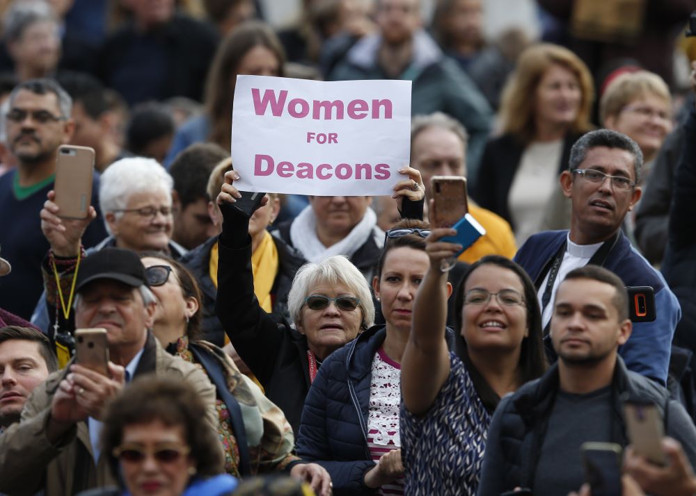 A woman holds a sign in support of women deacons.