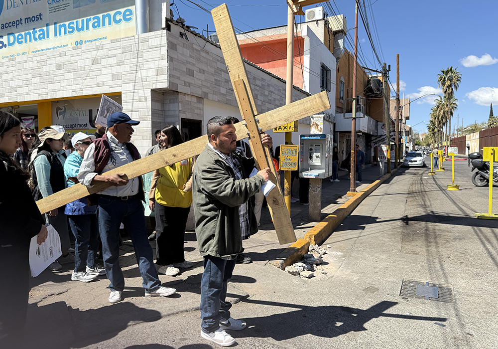 A huge wooden cross is carried on April 5 through the street that runs parallel to the border wall in Nogales, Mexico, during a symbolic Via Crucis acknowledging the indignities suffered by migrants trying to get to the United States. (Anita Snow)