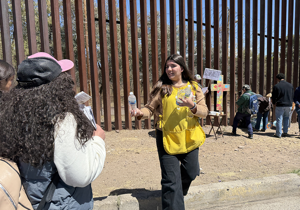 Ariane Trueba, a volunteer with the Kino Border Initiative, distributes bottles of water on April 5 to members of a Via Crucis procession the center organized along the border wall in Nogales, Mexico. (Anita Snow)