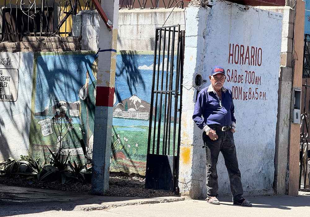 A man stands outside a business in Nogales, Mexico, on April 5 while watching a Via Crucis procession pass through the street facing the border wall. (Anita Snow)