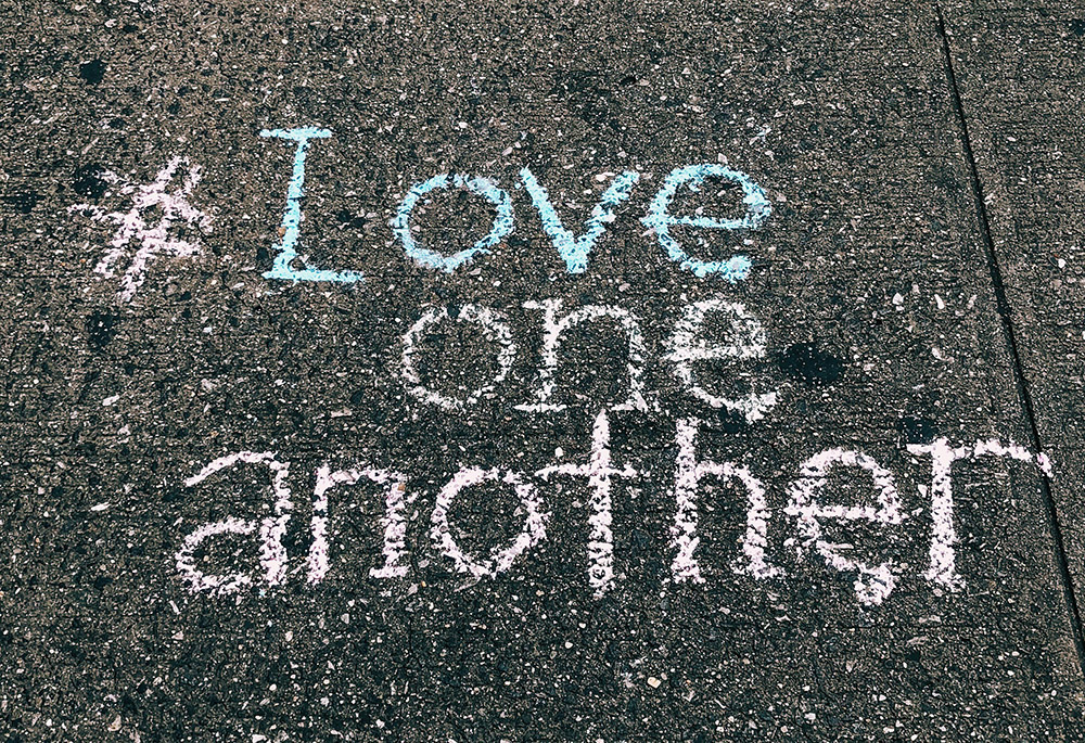 A concrete floor displays the words "#Love one another" written in chalk (Unsplash/Jon Tyson)