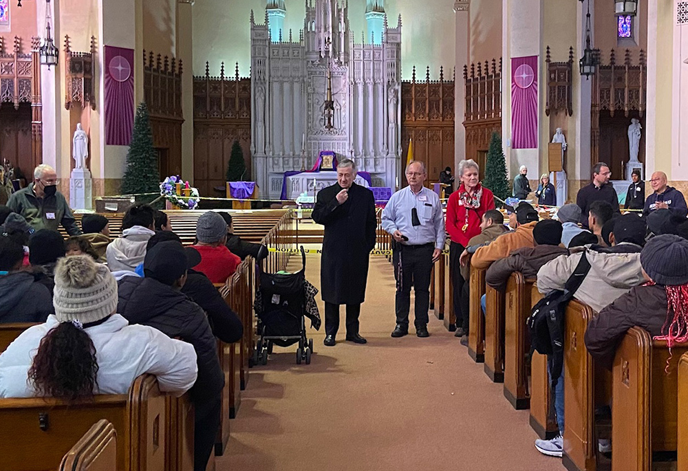Cardinal Blase Cupich of Chicago addresses migrants at the Migrant Ministry of the Catholic Parishes of Oak Park's first location at St. Catherine of Siena-St. Lucy Church in Oak Park, Illinois, in a December 2023 photo. Program organizer Celine Woznica is pictured at right. (Courtesy of Migrant Ministry)