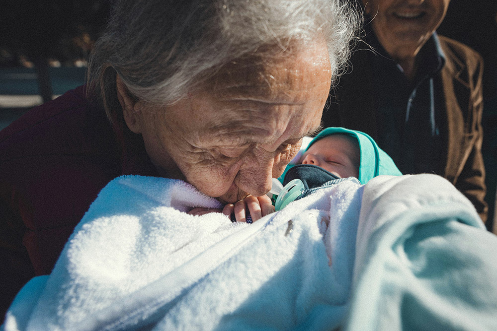 Grandmother kisses a baby on the hand (Unsplash/Tamara Govedarovic)
