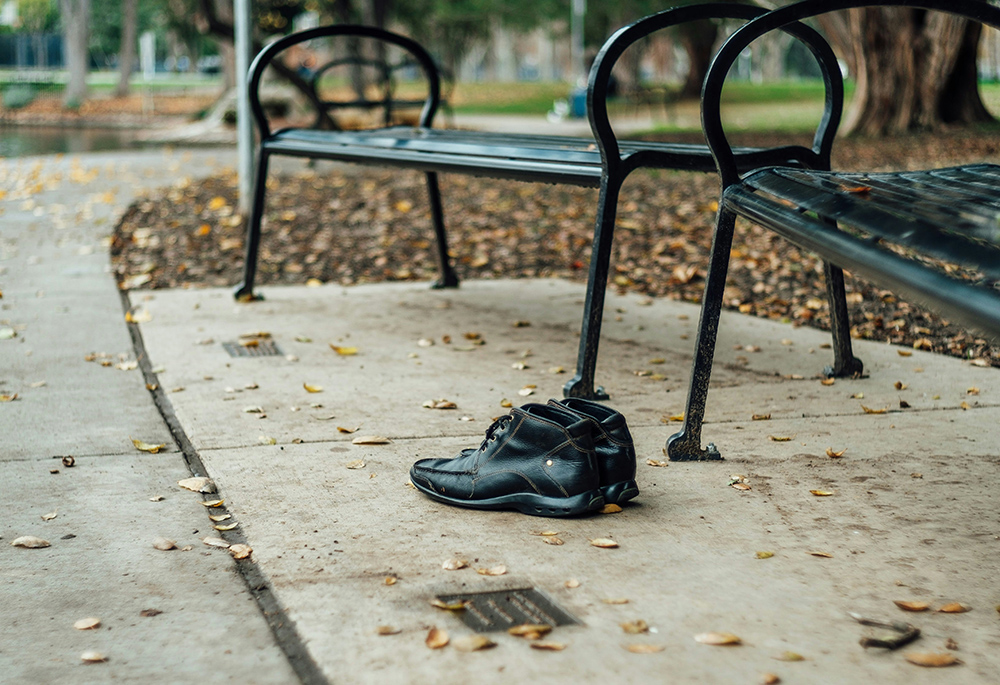 A pair of black shoes is pictured near two benches in a park setting. (Unsplash/Thomas Le)