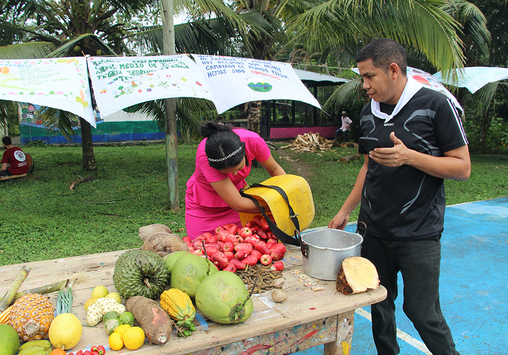 Council member Miguel Cepeda, right, is pictured with Nevaith Vargas, sharing fruits of their harvests on a common table at the cancha, the expansive ball court that doubled as a community gathering place, for the anniversary gathering. (Tracy L. Barnett)