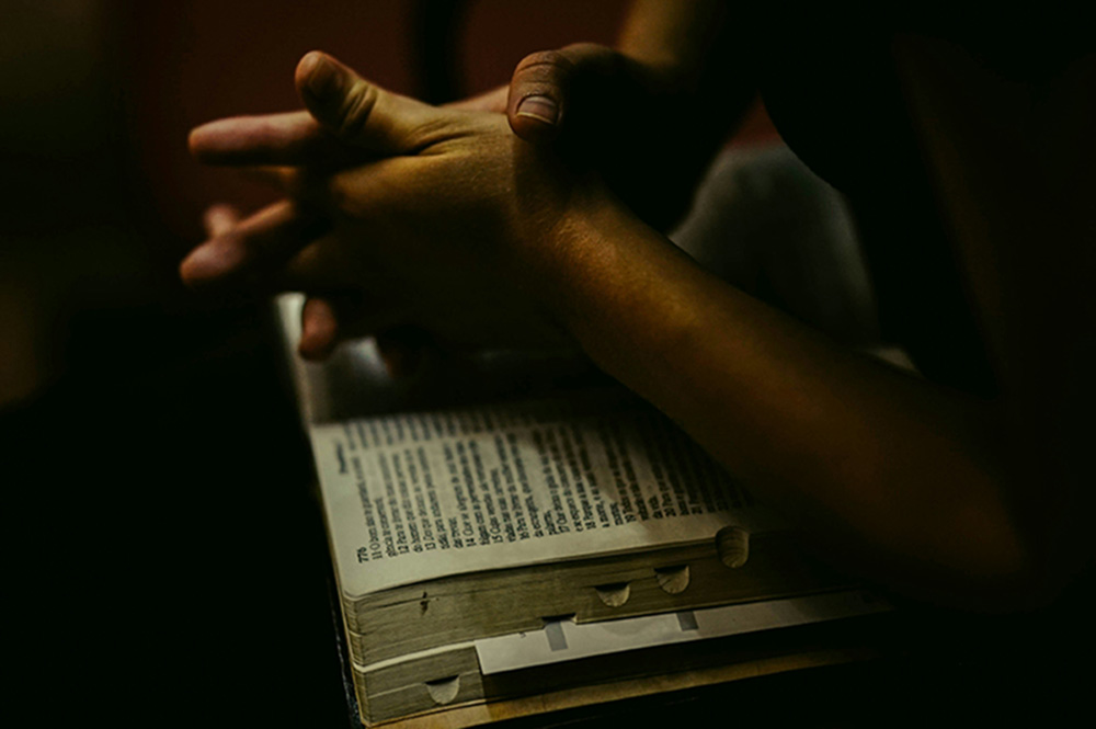 Hands clasped over a bible (Unsplash/Yohan Joy)