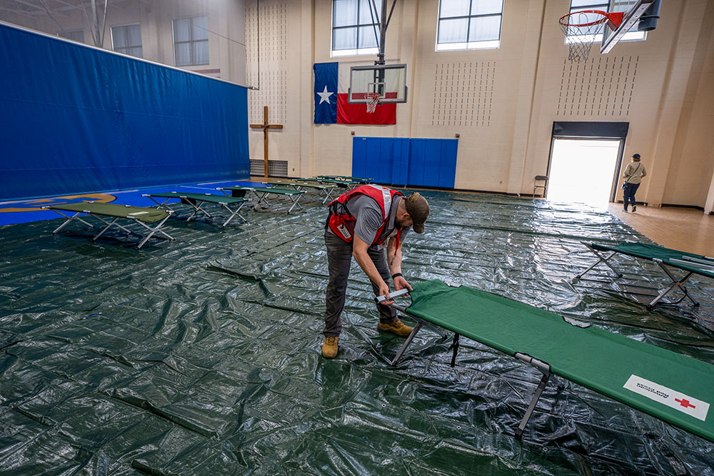 Randy Hughart, senior community disaster program manager for the American Red Cross of Central and South Texas, sets up cots in the Notre Dame Catholic School gym in Kerrville Texas. The Red Cross expects to house up to 10 families for at least a month in this location with one side of the gym providing sleeping space and the other side used for dining. (GSR photo/Gregg Brekke)