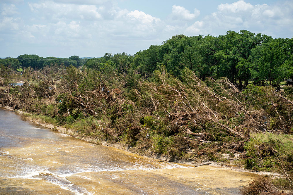 A grove of trees adjacent to a riverfront park and the Guadalupe River in Kerrville, Texas, was flattened during flash flooding July 4, 2025. Upstream debris litters the downed trees where search and rescue teams are just beginning to look for the remains of people washed away by the flood. (GSR photo/Gregg Brekke)