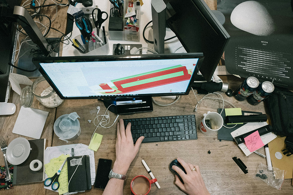 Someone working at a crowded desk on a computer (Unsplash/Robert Bye)