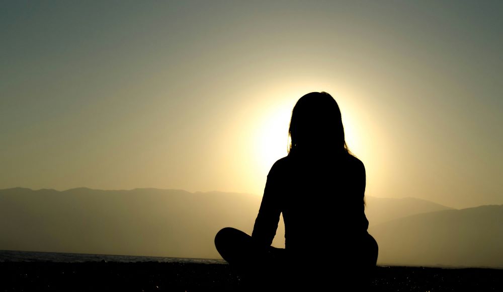 Person sits cross-legged watching sunset. Person sits cross-legged watching sunset.
