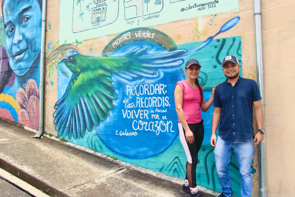 Luz Marina Betancur and Robinson Andrés Montes. The mural behind them reads, "Remember: from the Latin recorderis, which means to pass through the heart again. — Eduardo Galeano" (Tracy L. Barnett)