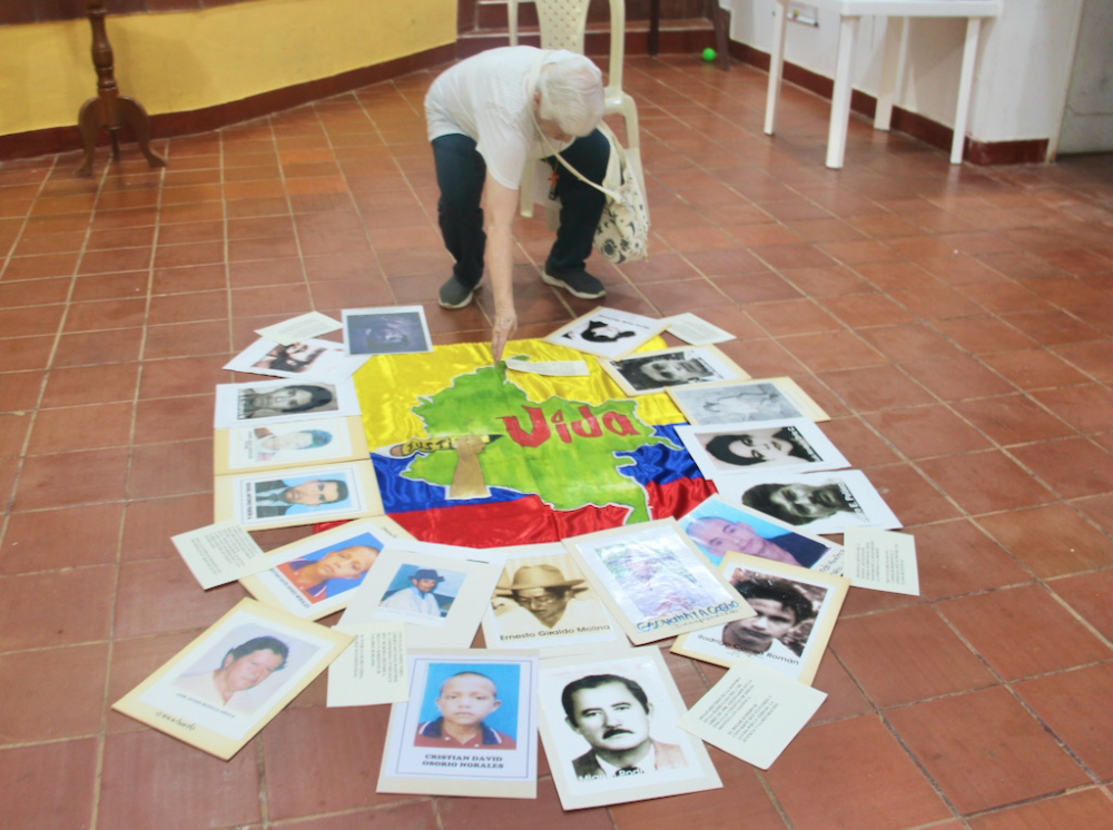 Sr. Maritze creates an altar from photos of Trujillo's many victims, with a banner proclaiming "Justice" and "Life" emblazoned on a map and flag of Colombia.
