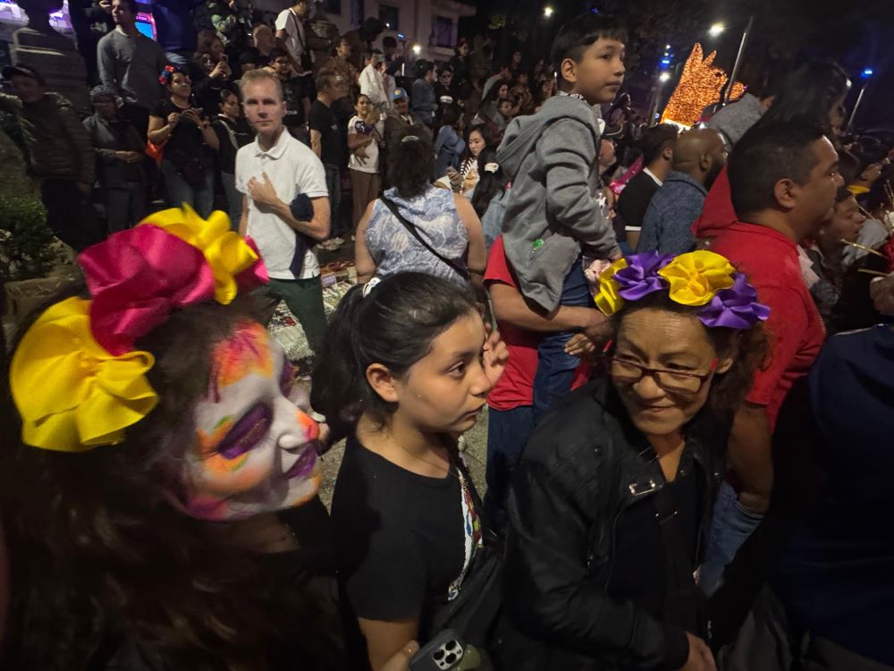 A trio of women gather Oct. 25 to watch participants of the Catrina Parade down Mexico City's grandest street, the Paseo de la Reforma, dressed as skeletons.