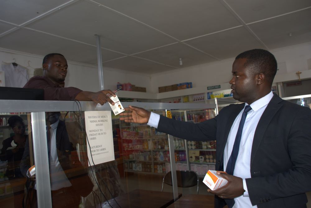 Man at counter hands receipt to man who picked up a prescription. 