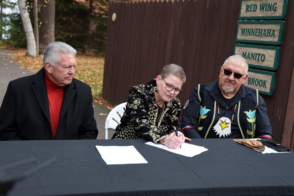 2 men look on as Sr. Sue Ernster signs title documents for property the Franciscan Sisters of Perpetual Adoration had owned Oct. 31. 