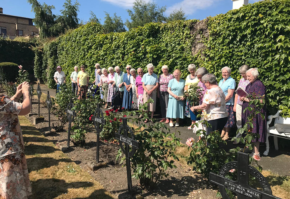 Sr. Jane Livesey, former superior general of the Congregation of Jesus, puts flowers on her great-aunt’s grave in the Loreto cemetery in Rathfarnham, Dublin, watched by Loreto sisters from Abbey House. A Vatican decree has granted the merger of the Congregation of Jesus and the Institute of the Blessed Virgin Mary. (Courtesy of Sr. Noelle Corscadden)