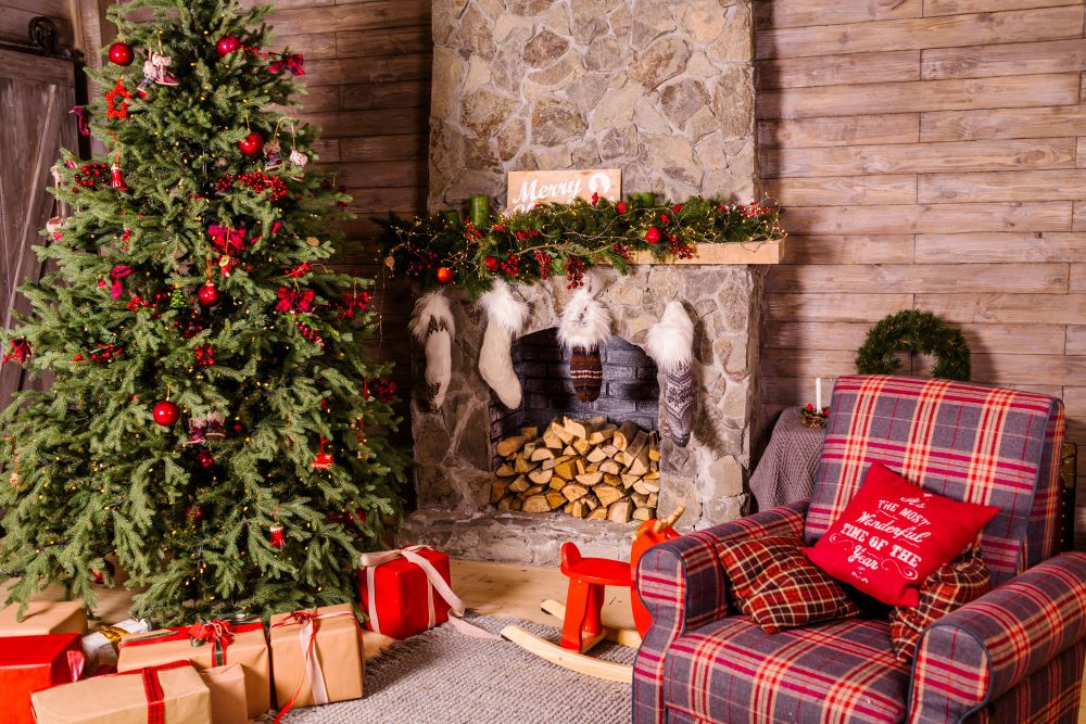 A Christmas tree with gifts underneath, near a fireplace with stockings