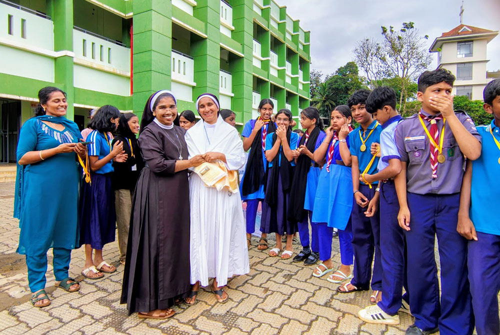 Adoration Sr. Sabina Joseph, in white habit, is honored by Carmelite of Mary Immaculate Sr. Siji M, headmistress of Dwaraka Upper Primary School, Mananthavady, for winning a gold medal in the State Masters Athletics Championship hurdles competition held on Oct 24, 2025, in a function at the school where Joseph teaches. (Courtesy of Sabina Joseph)