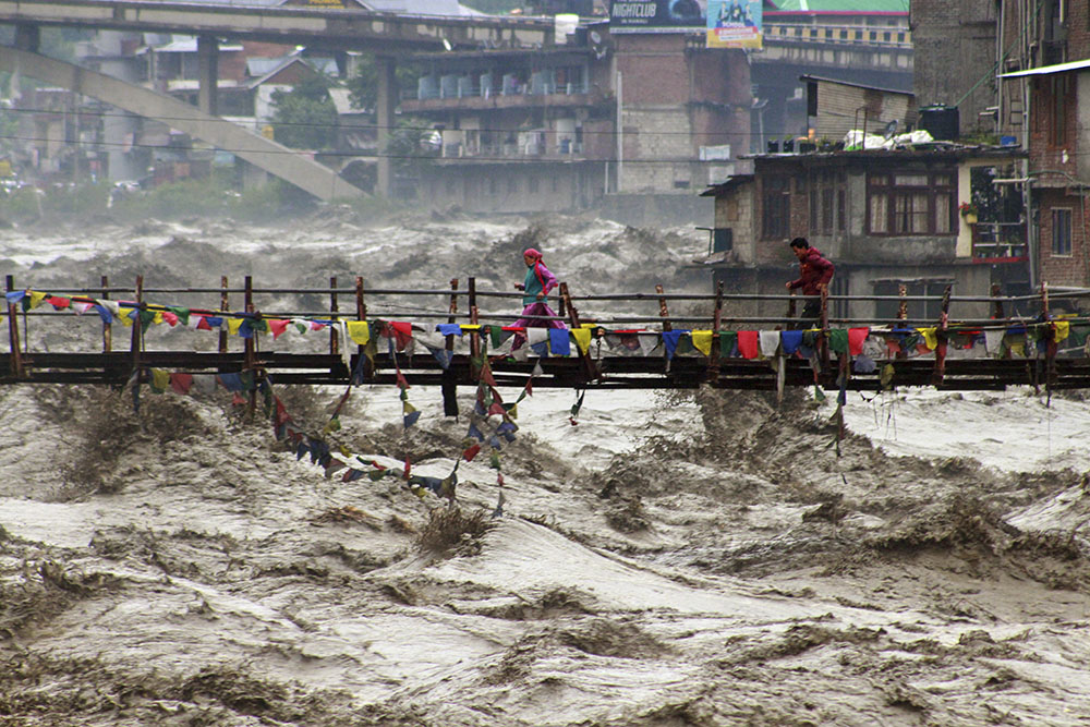 Residents run across a bridge over the flooding Beas River following incessant rains in Kullu, in northern Indian state of Himachal Pradesh, Aug. 26, 2025. (AP/Aqil Khan)