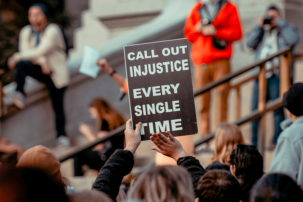 A sign reads, "Call out injustice every single time" (Unsplash/Colin Lloyd)