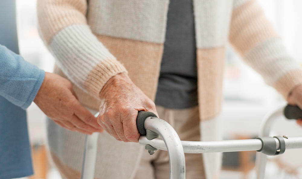 A person uses a walker with a health care worker assisting (Dreamstime/Yuri  Arcurs)