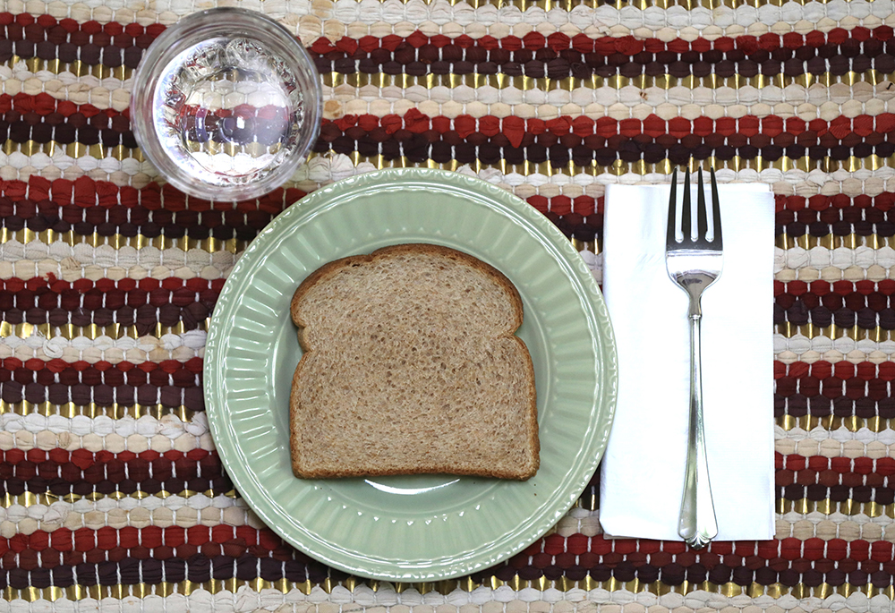 A slice of bread and glass of water are pictured in an illustration. "When I was in formation, I was taught to fast, especially from the things I love most at both the personal and community levels," writes Sr. Alice Nyazungu. (OSV News/Bob Roller)