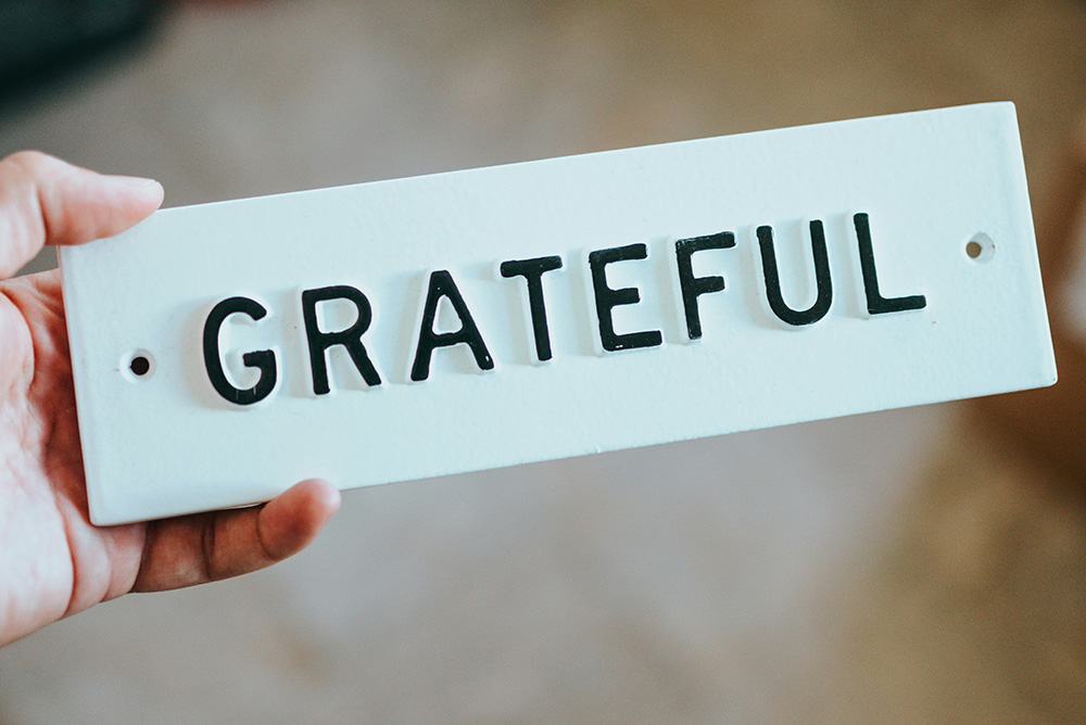 A white metal plate with the word GRATEFUL in raised black letters (Unsplash/Nathan Dumlao)