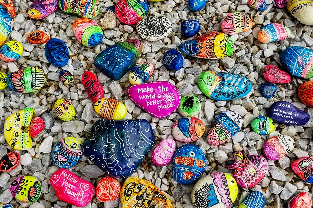 Painted stones with colorful fish and the messages "Make the world a better place" and "Follow your heart" (Unsplash/Simon Ray)